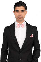 Man wearing a black suit with a white shirt and pink bow tie and pocket square on a white background