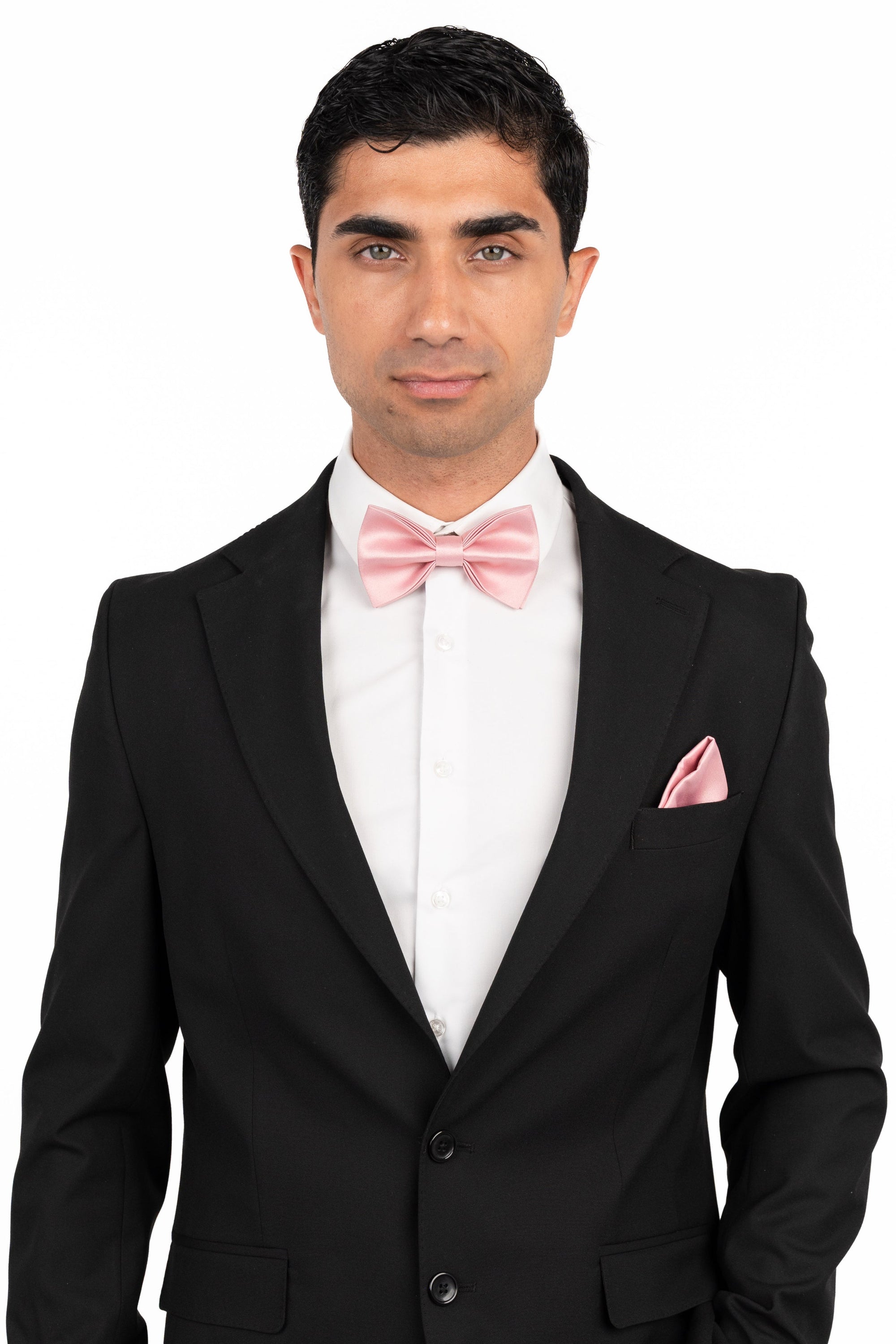 Man wearing a black suit with a white shirt and pink bow tie and pocket square on a white background