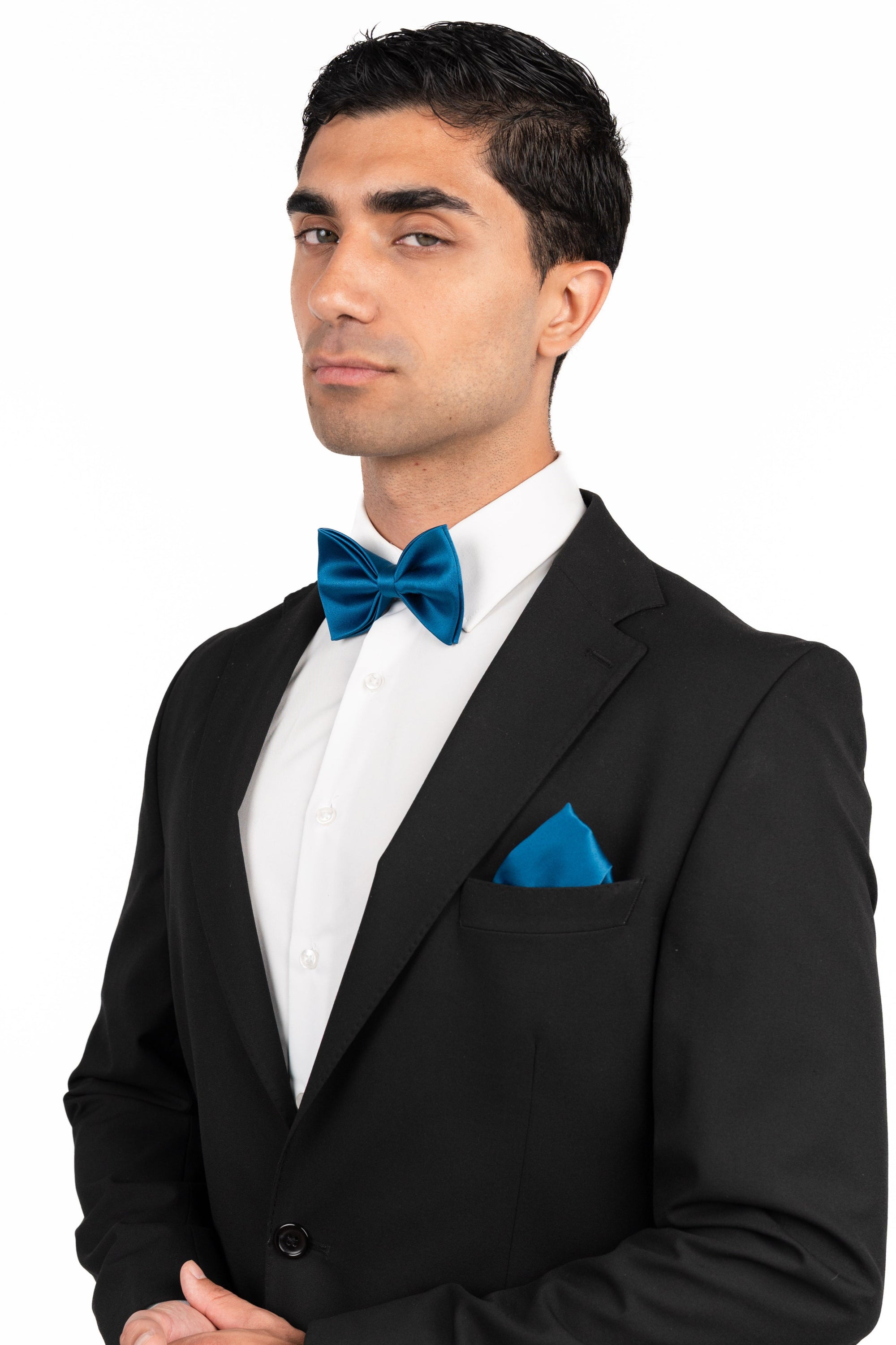 Man wearing a black tuxedo with a blue bow tie and pocket square on a white background