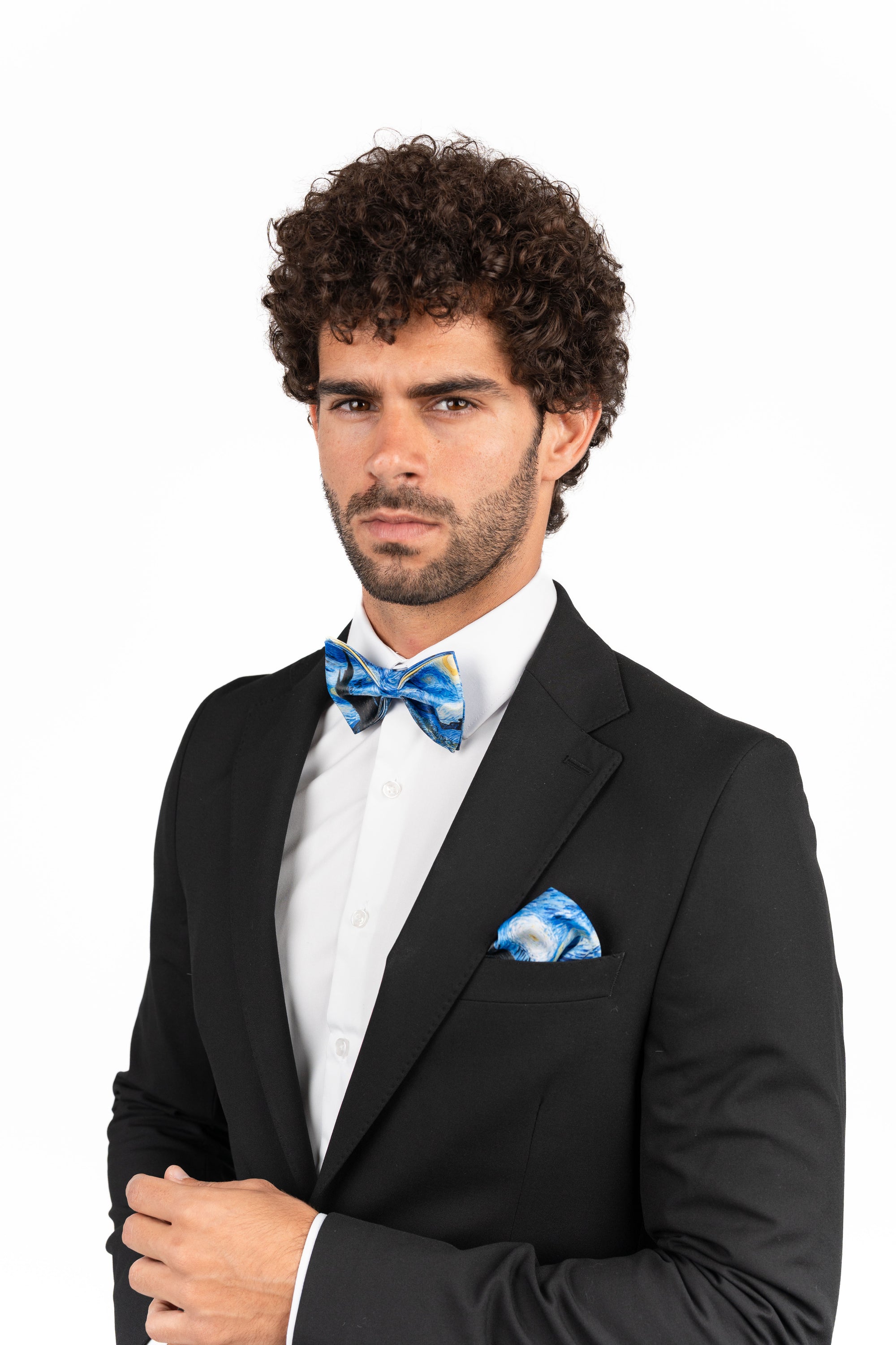 Man wearing a black suit with a blue bow tie and pocket square on a white background
