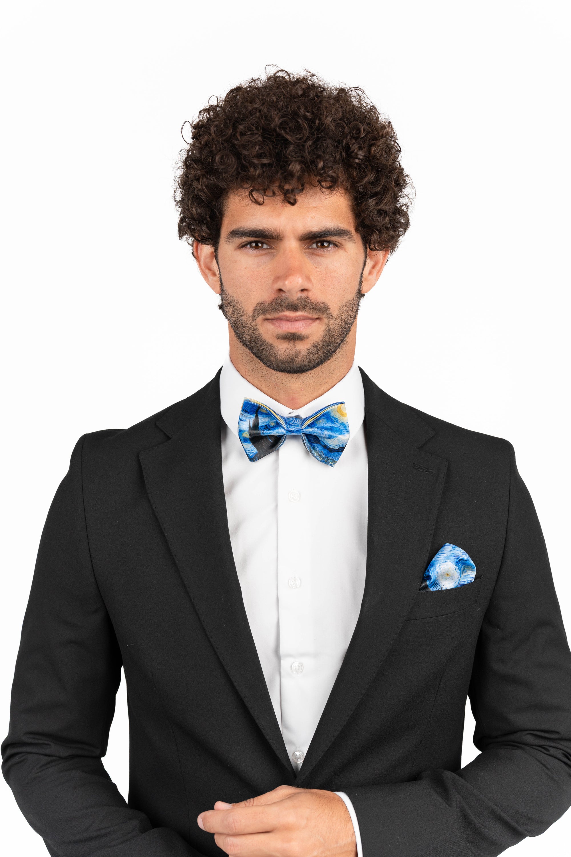 Man wearing a black suit with a blue bow tie and pocket square on a white background