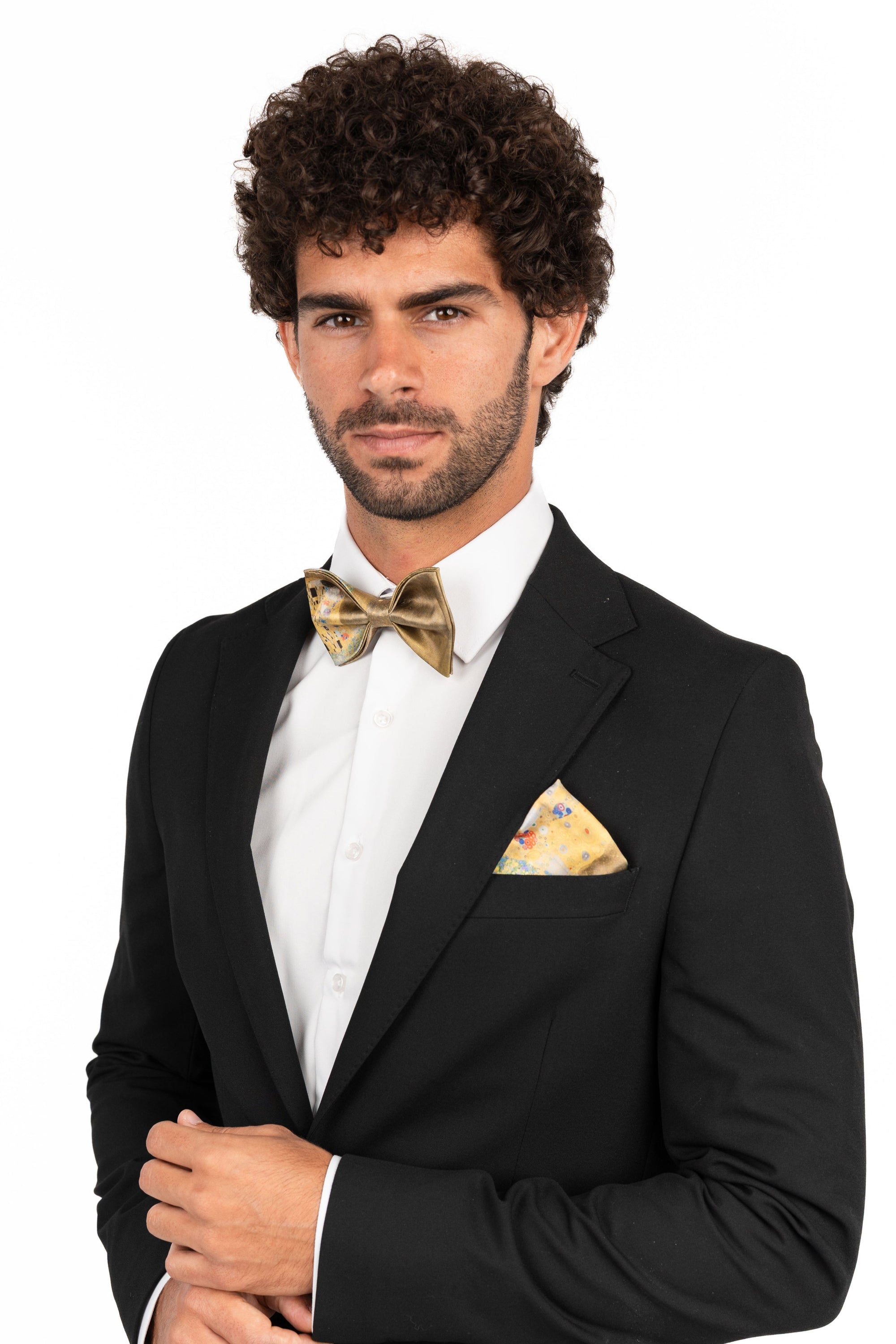 Man wearing a black suit with a white shirt, gold bow tie, and pocket square on a white background gustav klimt the kiss
