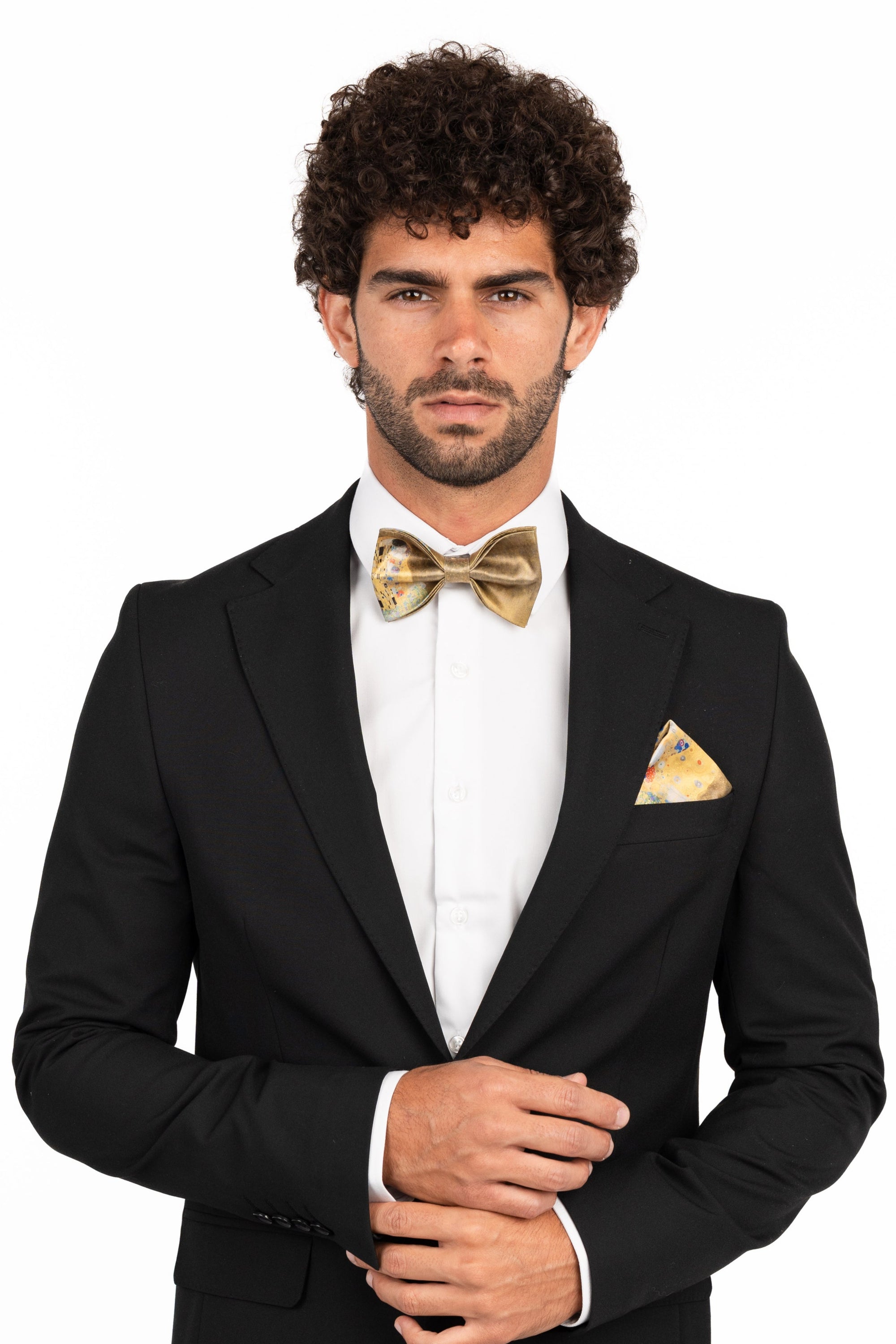 Man wearing a black suit with a white shirt and gold bow tie and pocket square on a white background