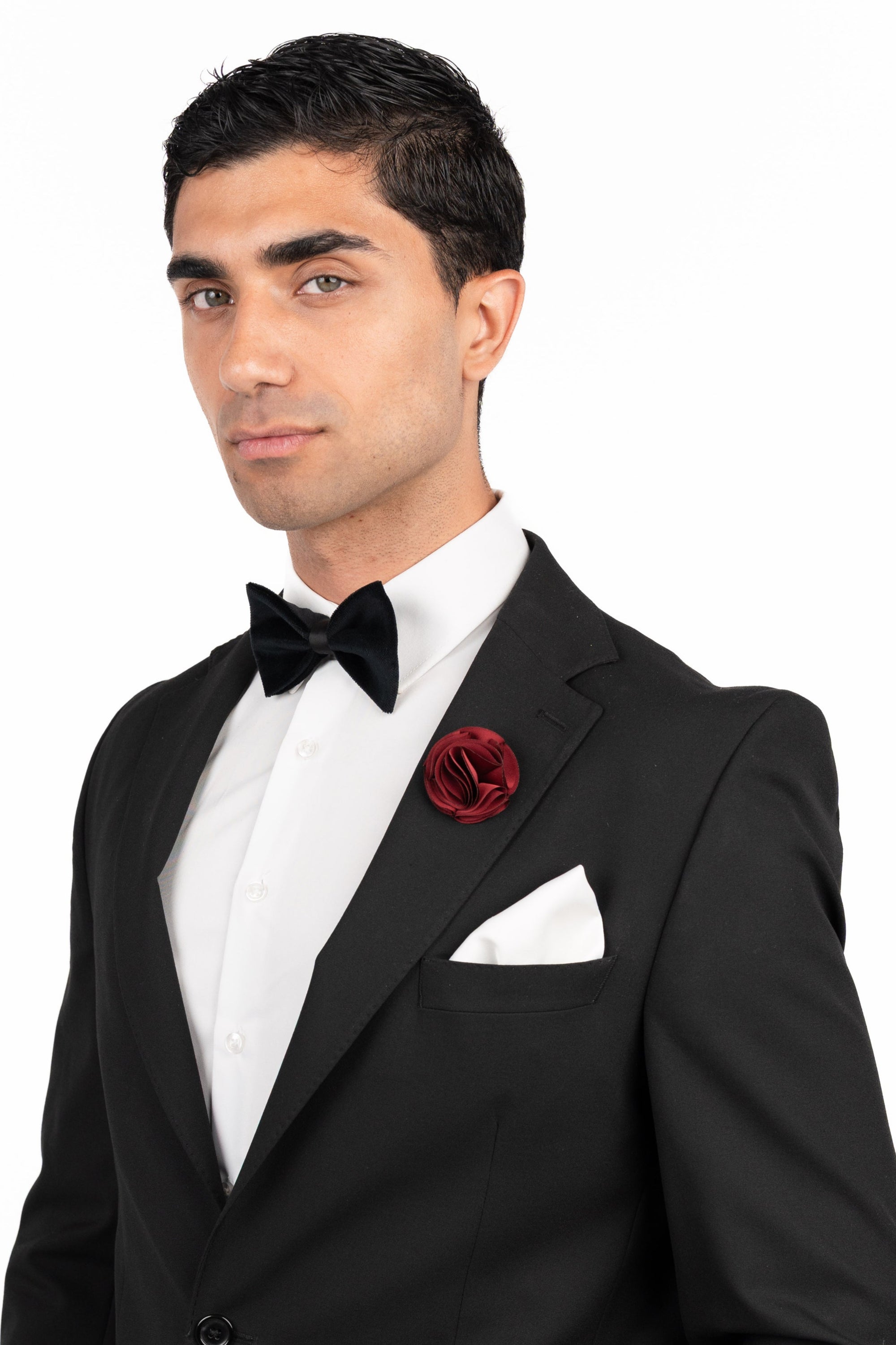 Man wearing a black tuxedo with a red boutonniere on a white background