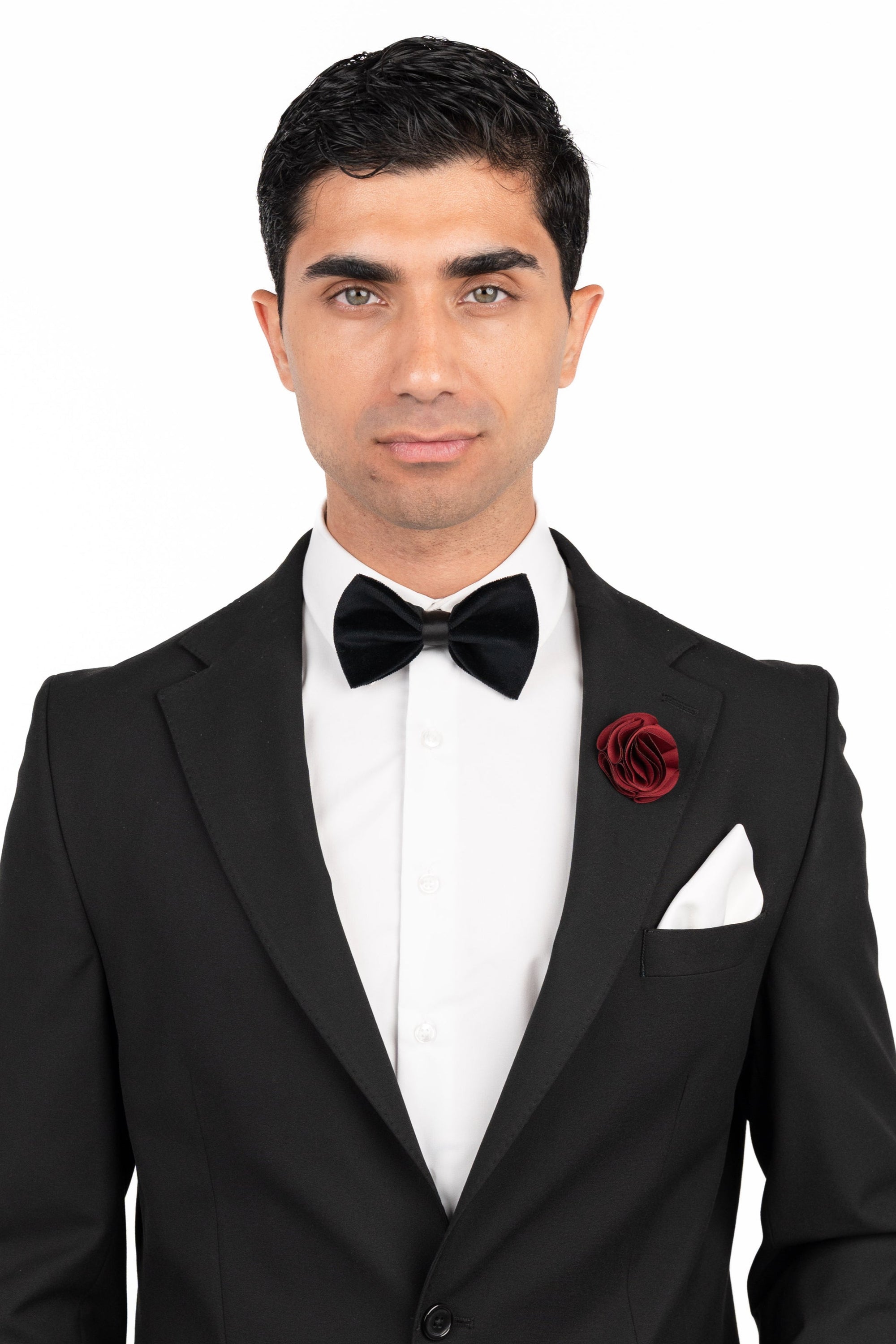 Man wearing a black tuxedo with a bow tie and red boutonniere on a white background