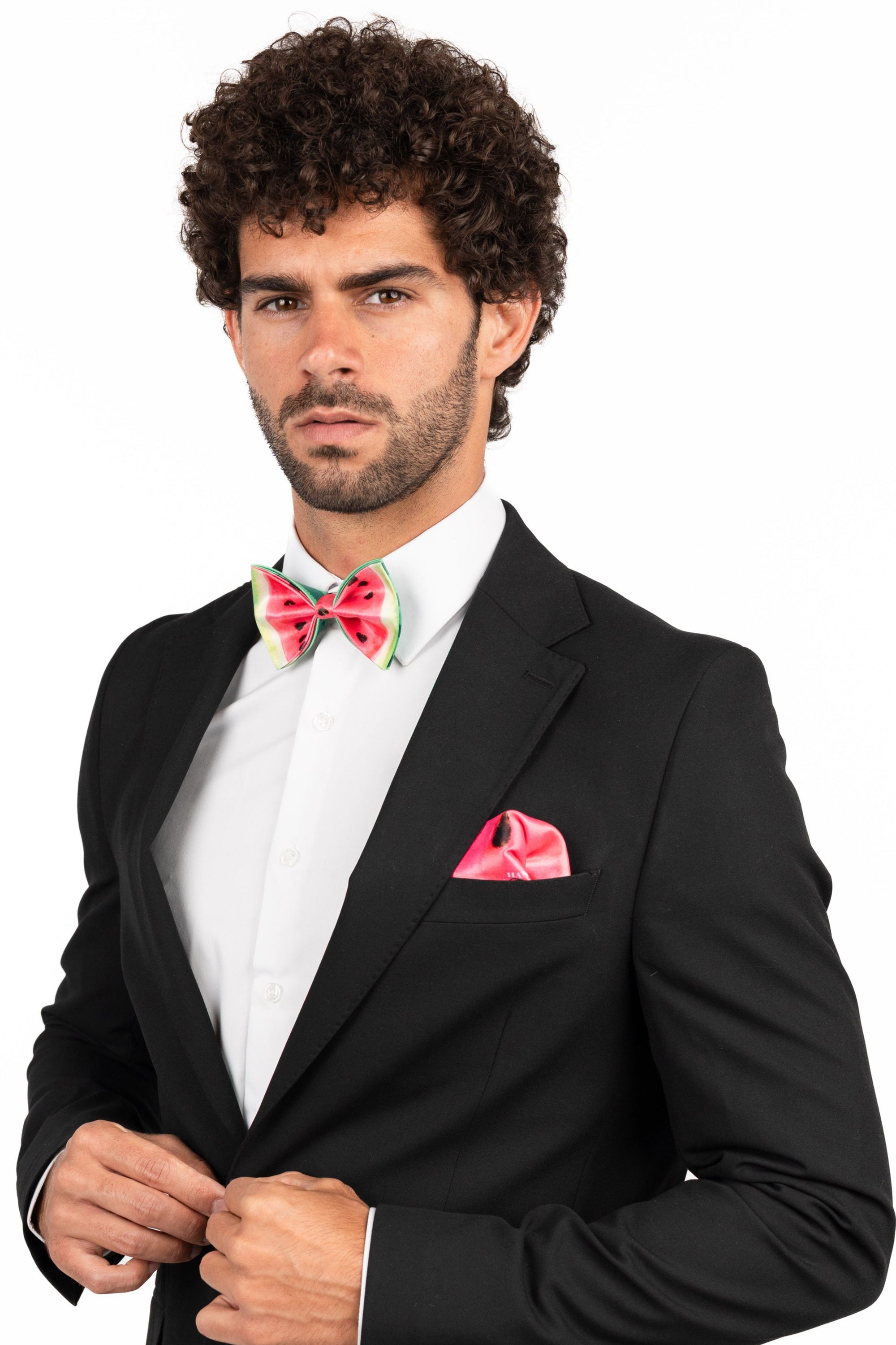 Man wearing a black suit with a white shirt, red bow tie, and pink pocket square on a white background