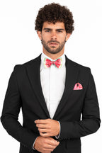 Man wearing a black suit with a white shirt, colorful bow tie, and pink handkerchief on a white background