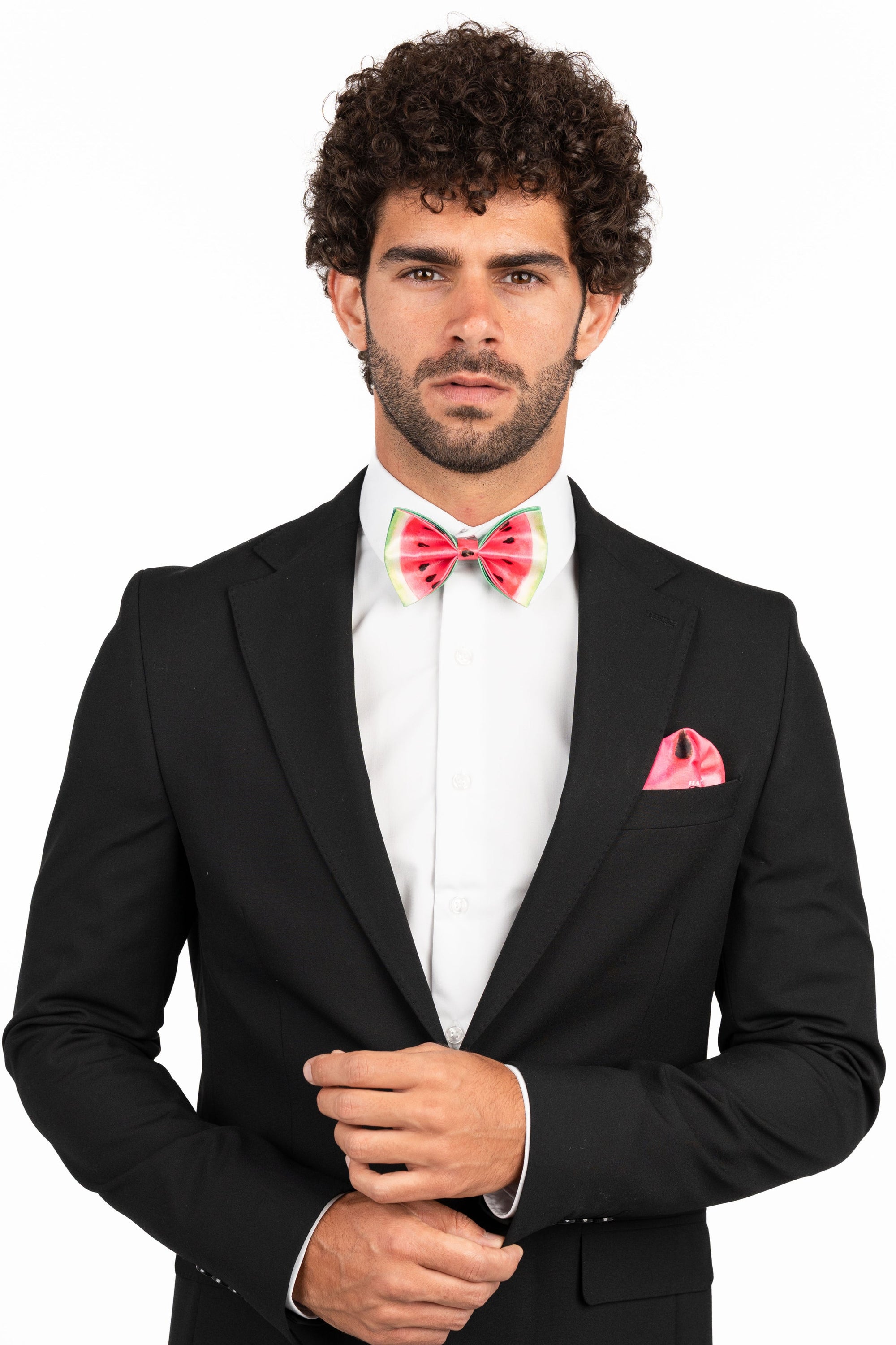 Man wearing a black suit with a white shirt, colorful bow tie, and pink handkerchief on a white background