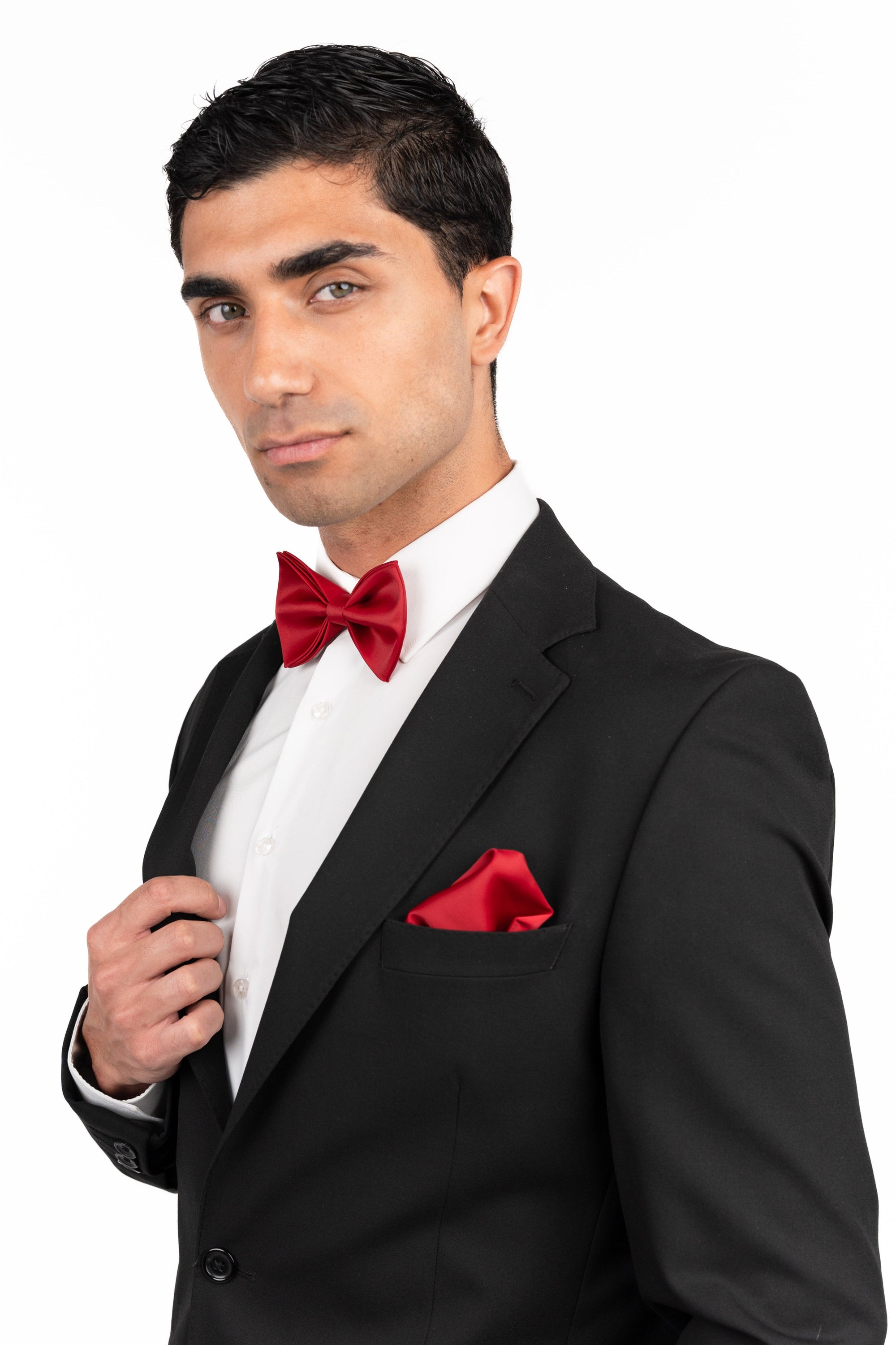Man in a black tuxedo with a red bow tie and pocket square on a white background