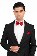 Man wearing a black suit with a red bow tie and pocket square on a white background
