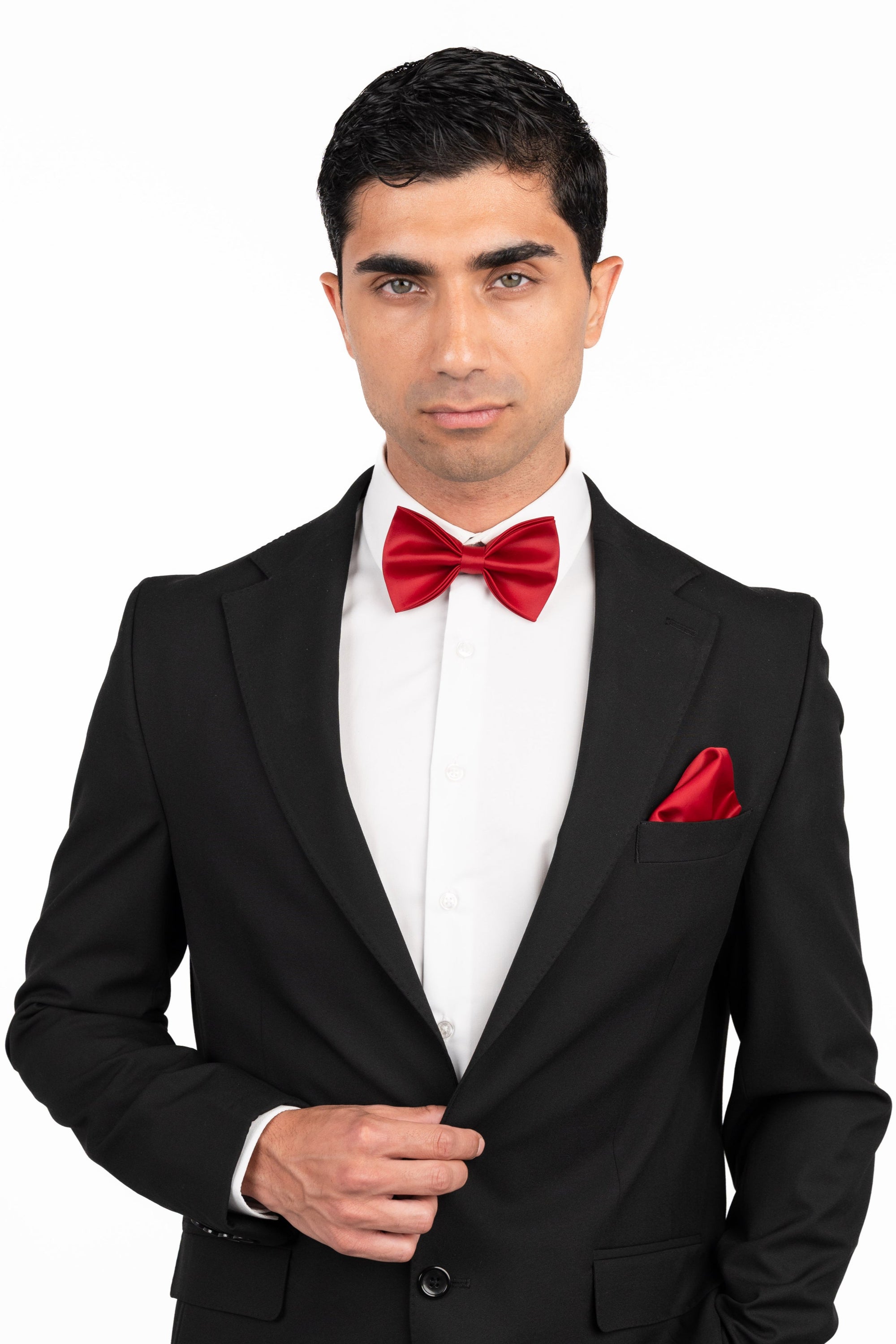 Man wearing a black suit with a red bow tie and pocket square on a white background